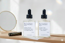 Elodie's Naturals: Two clear dropper bottles beside a round mirror