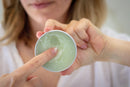 Elodie's Naturals: Woman touching balm in open tin